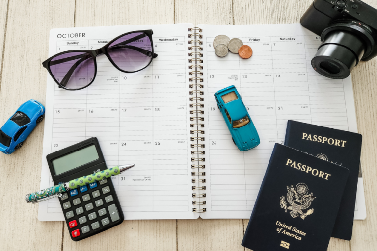 Sunglasses, camera, toy cars, loose change, passports and calculator on top of planner