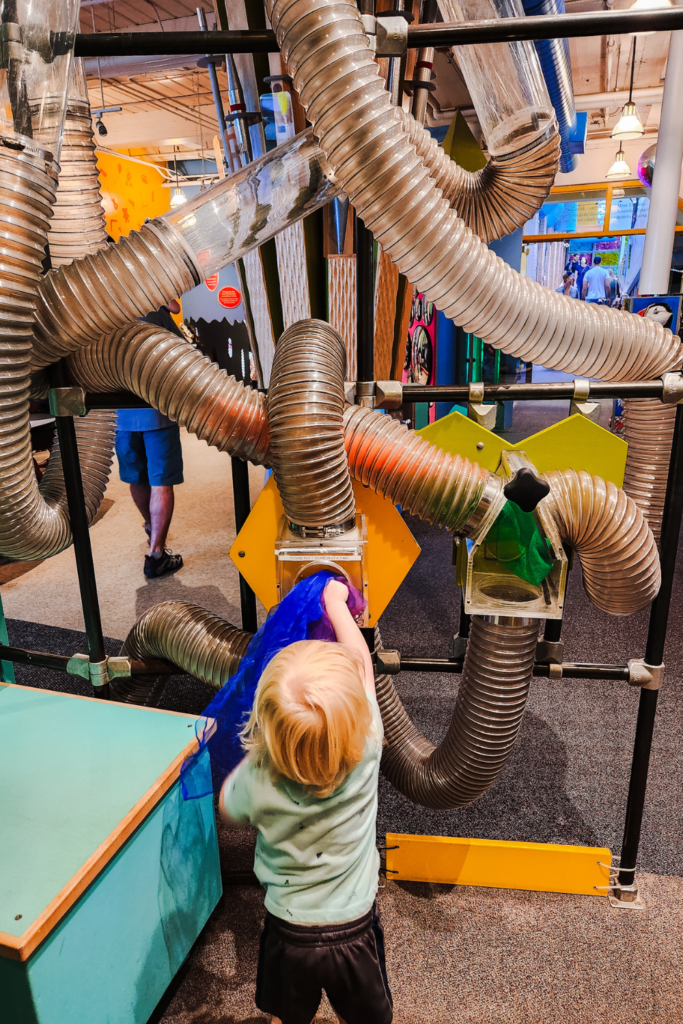 Child putting scarves in air tubes at Providence Children's Museum